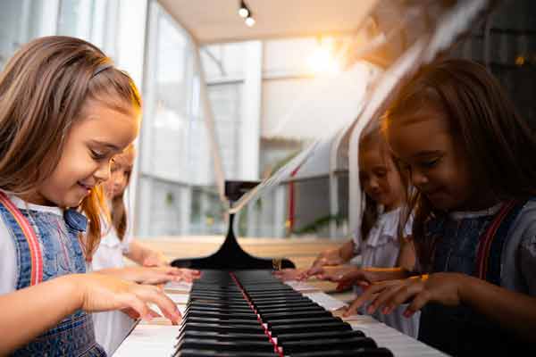 Fille souriante jouant à 4 mains sur un piano